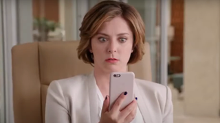 Rebecca looks shocked as she checks a text on her phone.