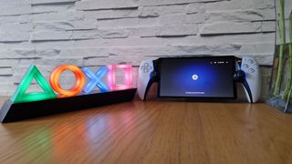 A photo of the PlayStation Portal handheld gaming device on a wooden table alongside some PlayStation themed lights.