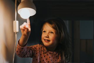Cute young girl in pyjamas, in the dark, smiling and pointing at a little night light