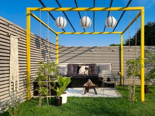 a painted yellow pergola in a modern garden with black seating and grey fences