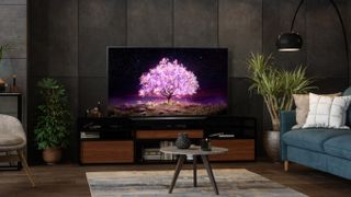 LG C1 OLED-Fernseher auf einem TV-Ständer in einem unübersichtlichen, aber gemütlichen Wohnzimmer mit Pflanzen in der Nähe 