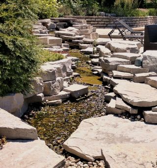 a natural garden water feature of natural stone gradually sloping alongside a patio