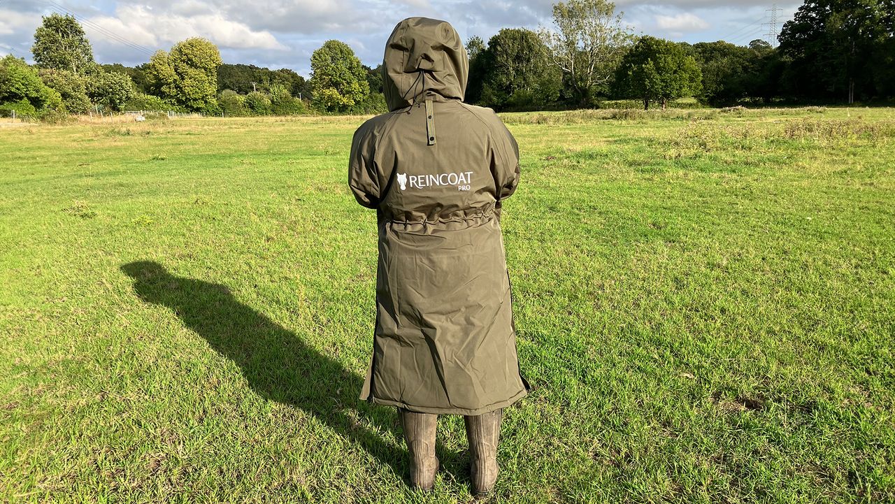 Lady wears Reincoat Pro in a field with hood up, viewed from the back