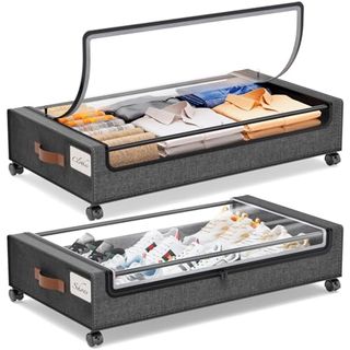 Two gray fabric under bed storage containers on wheels with clear zip lids. Folded clothes and shoes inside. 