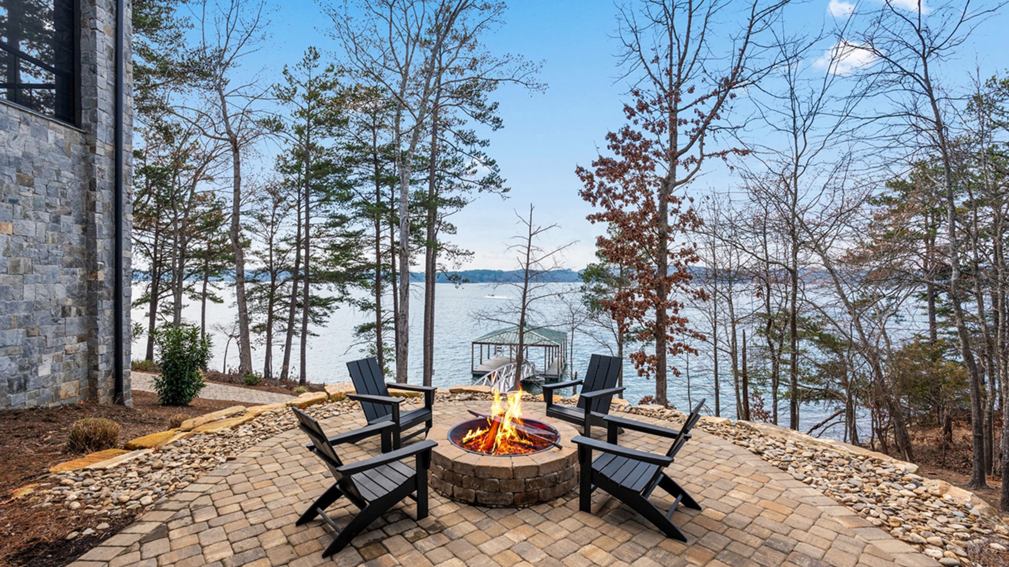 Chairs circle a firepit at a home on a lake