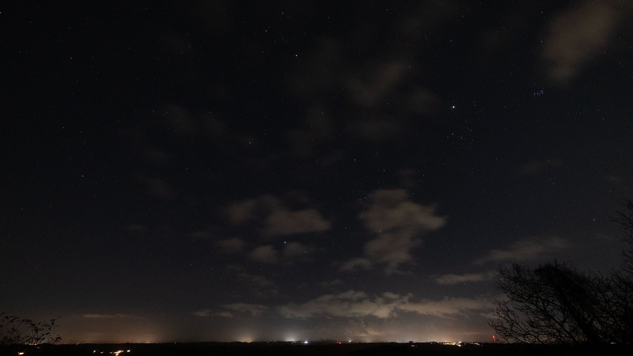 Orion and the Pleiades in the night sky with clouds and light pollution