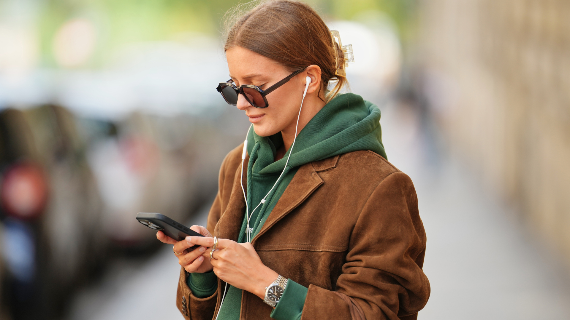  Diane Batoukina wears light brown hair styled in a low bun, oversized square sunglasses by Kaleos, a brown suede leather blazer jacket, a green WRSTBHVR hoodie with white printed logo, during a street style fashion photo session, on September 05, 2025 in Paris, France. (Photo by Edward Berthelot/Getty Images)