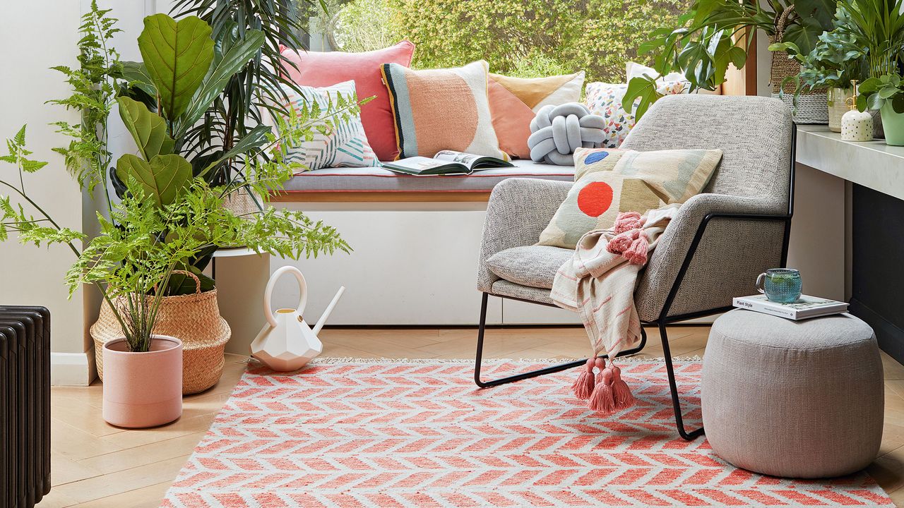 White living room with window seat covered in cushions with coral and white rug in front