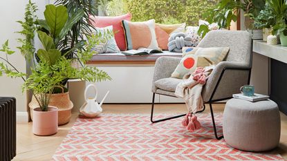 White living room with window seat covered in cushions with coral and white rug in front