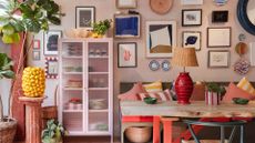 A colorful living space with a gallery wall, a sofa decked out in striped pillows, a glass storage cabinet in blush pink and plenty of colorful decor