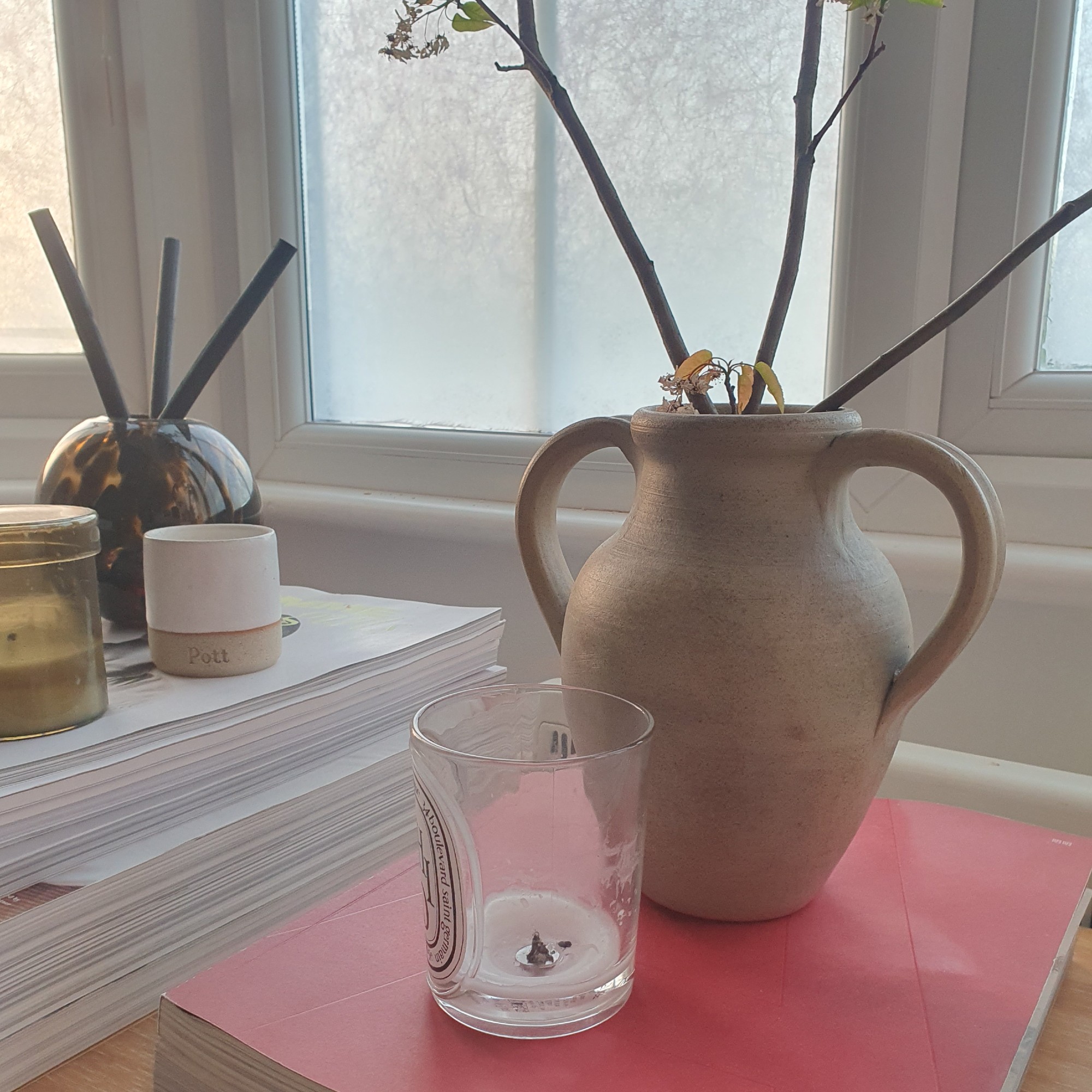Finished Shiso candle from Diptyque on Sara Hesikova's sideboard next to a vase filled with branches