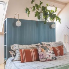 Bed with large blue wooden headboard with storage in it and sconce lighting hanging from it