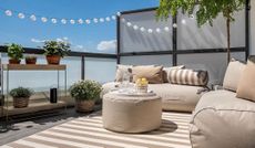 Bright outdoor rooftop/appartment space with white outdoor couches, center table and shelving