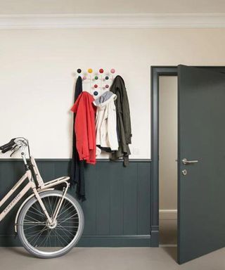 A hallway with half heigh wainscotting, a bike and coats hanging on the wall above