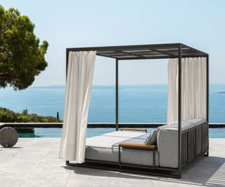 A pergola day bed next to a pool with outdoor curtains hanging from the rafters