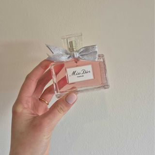 A close-up of Digital Beauty Writer, Naomi Jamieson's hand holding up Dior's Miss Dior perfume against a cream wall