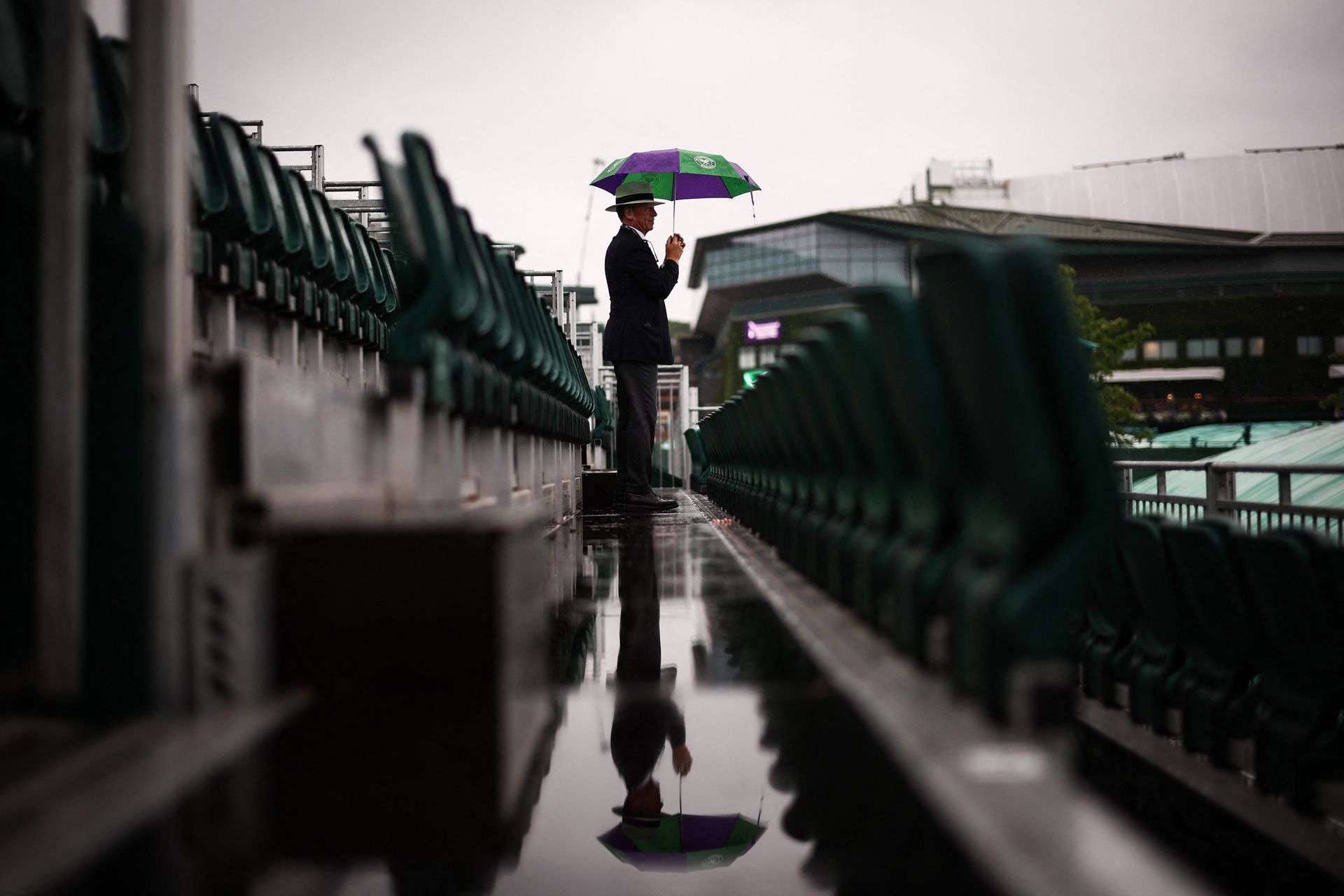 
                                A staff member stands under an umbrella during the 2025 Wimbledon Championships in London
                            