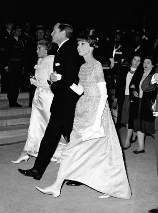 Audrey Hepburn wears a short-sleeve dress and flats, pictured with two other people.