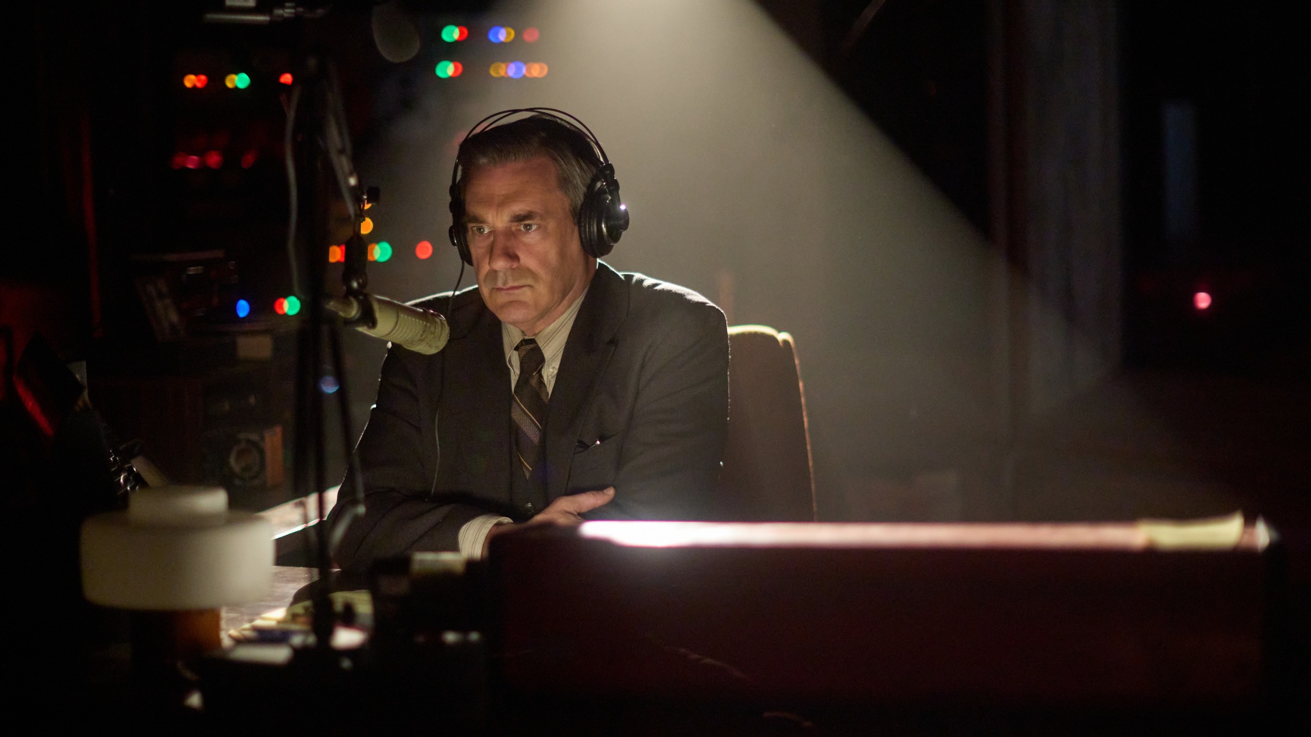 Jon Hamm as Fred Heckman sitting in front of a microphone at a radio station.