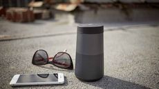 Bose SoundLink Revolve Bluetooth speaker outside on floor with sunglasses and phone