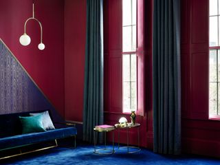 A deep red living room with blue carpet and a velvet blue sofa, with red shutters over the window