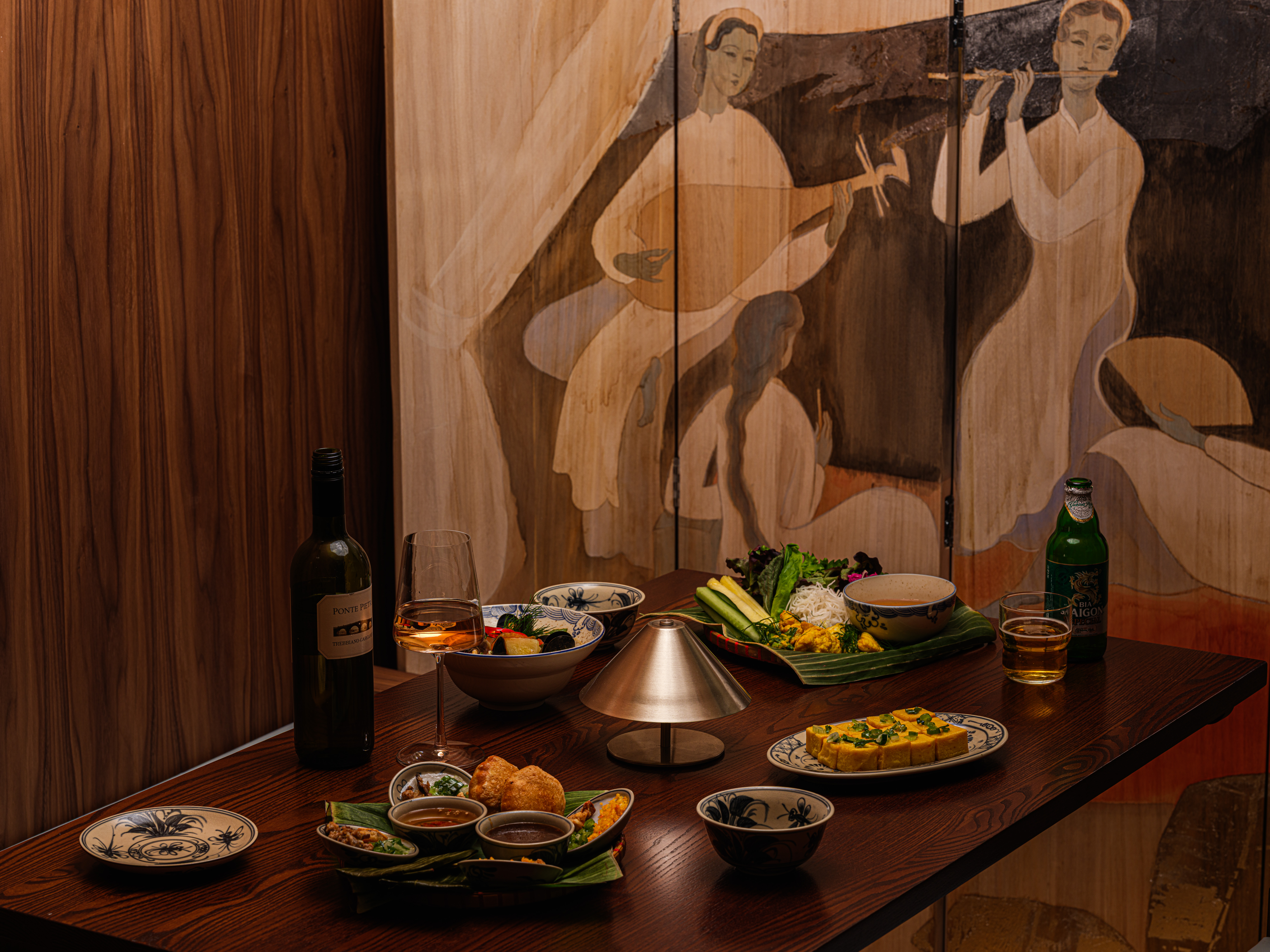 A dramatically lit and designed restaurant pairing cement walls with hand-painted wooden panels, murals, terracotta tiles, chrome accents, and glass blocks.