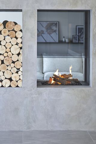 A concrete wall with glass fireplace and stack of logs