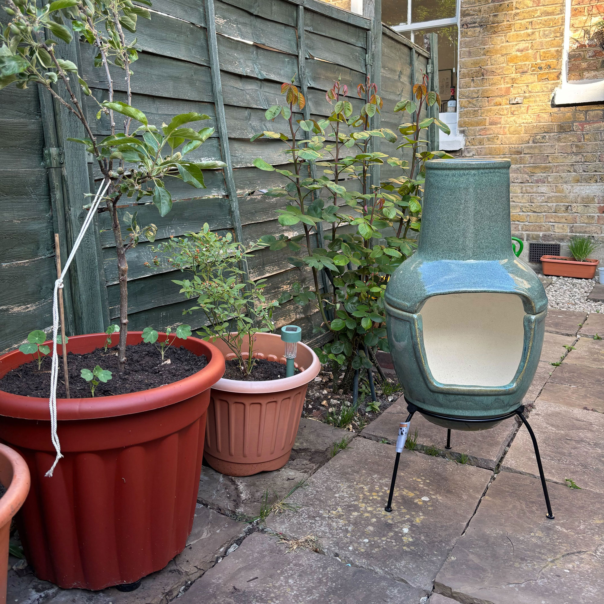 Green chiminea in a patio courtyard garden with a striped sofa