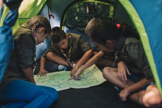 A group of kids inside a tent look intently at a map.