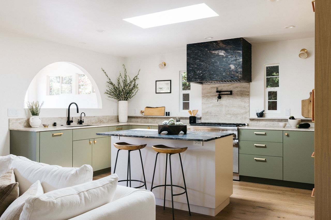 Short slab earthy colored backsplash in modern kitchen with black marble hood, island and sage green cabinet finish