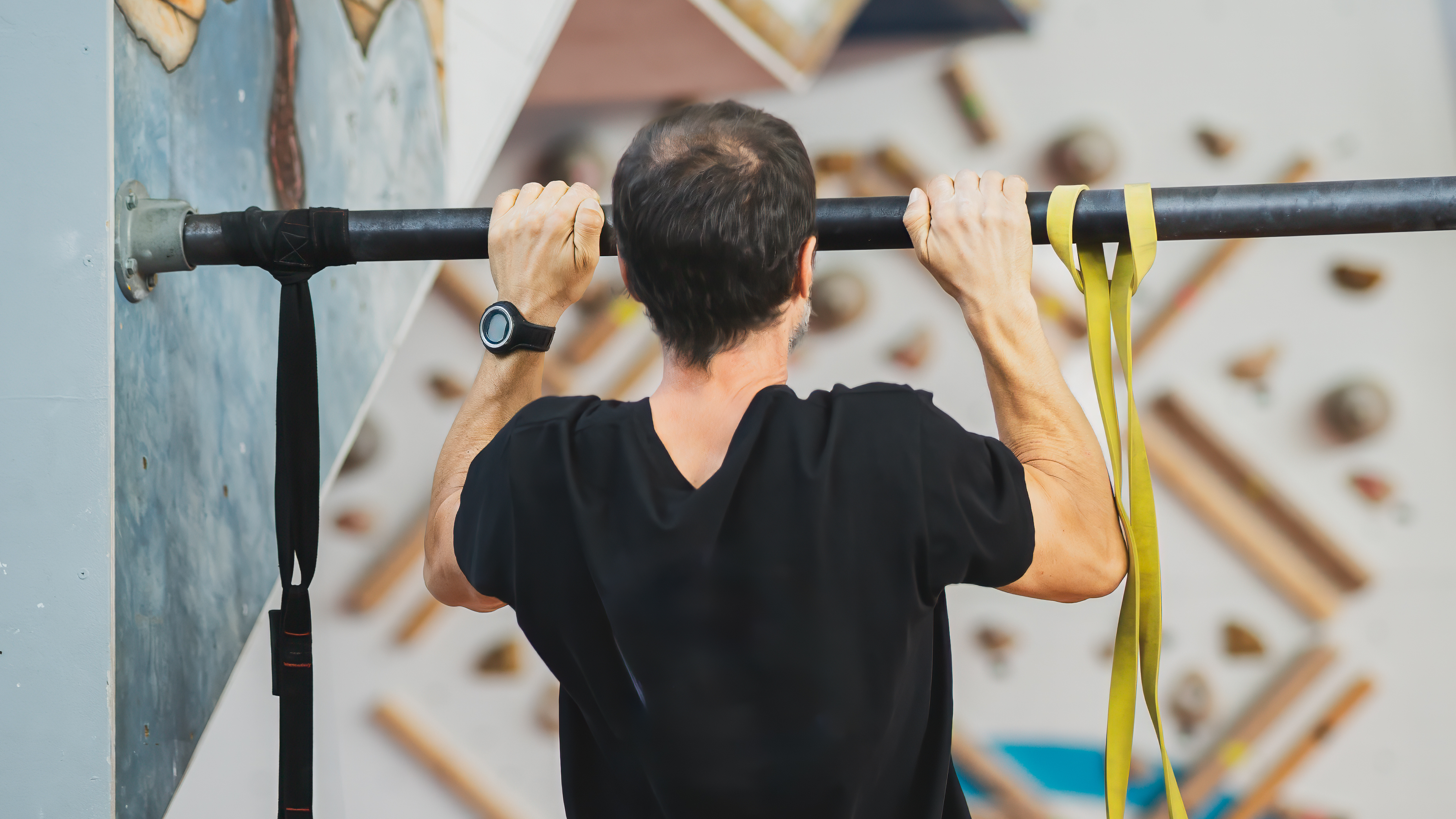Man performing pull-up on pull-up bar, a yellow resistance band is wrapped around the bar to his right