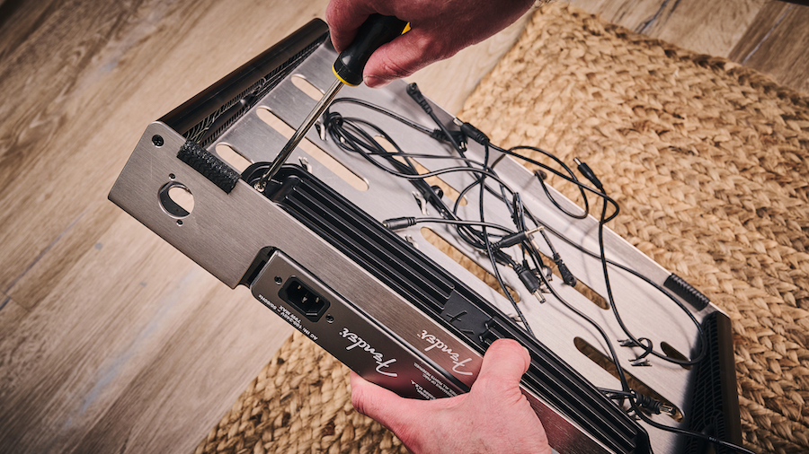 Man screwing a Fender power supply to the underside of a Fender pedalboard