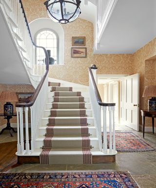 white staircase with neutral runner in hall with patterned wallpaper, globe light and patterned rugs