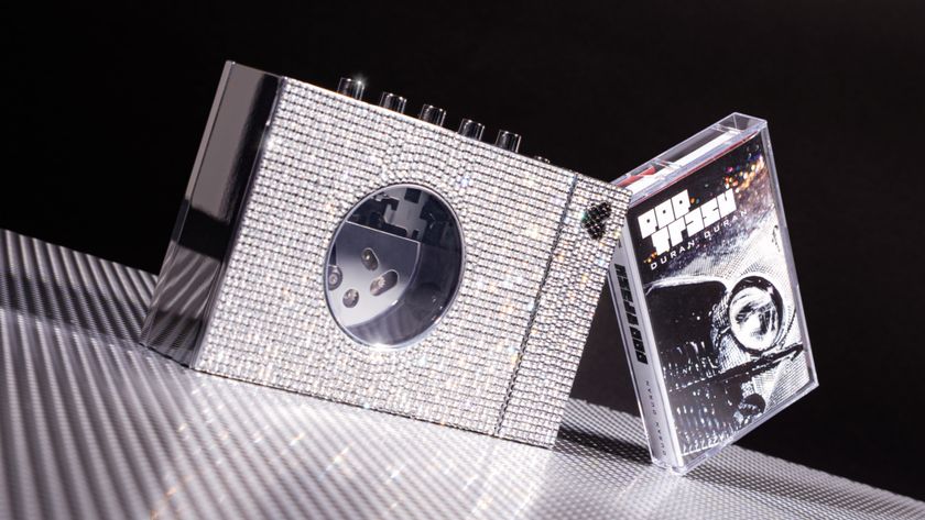 A jewel-encrusted Walkman with a cassette tape on silver metallic table, with dark background