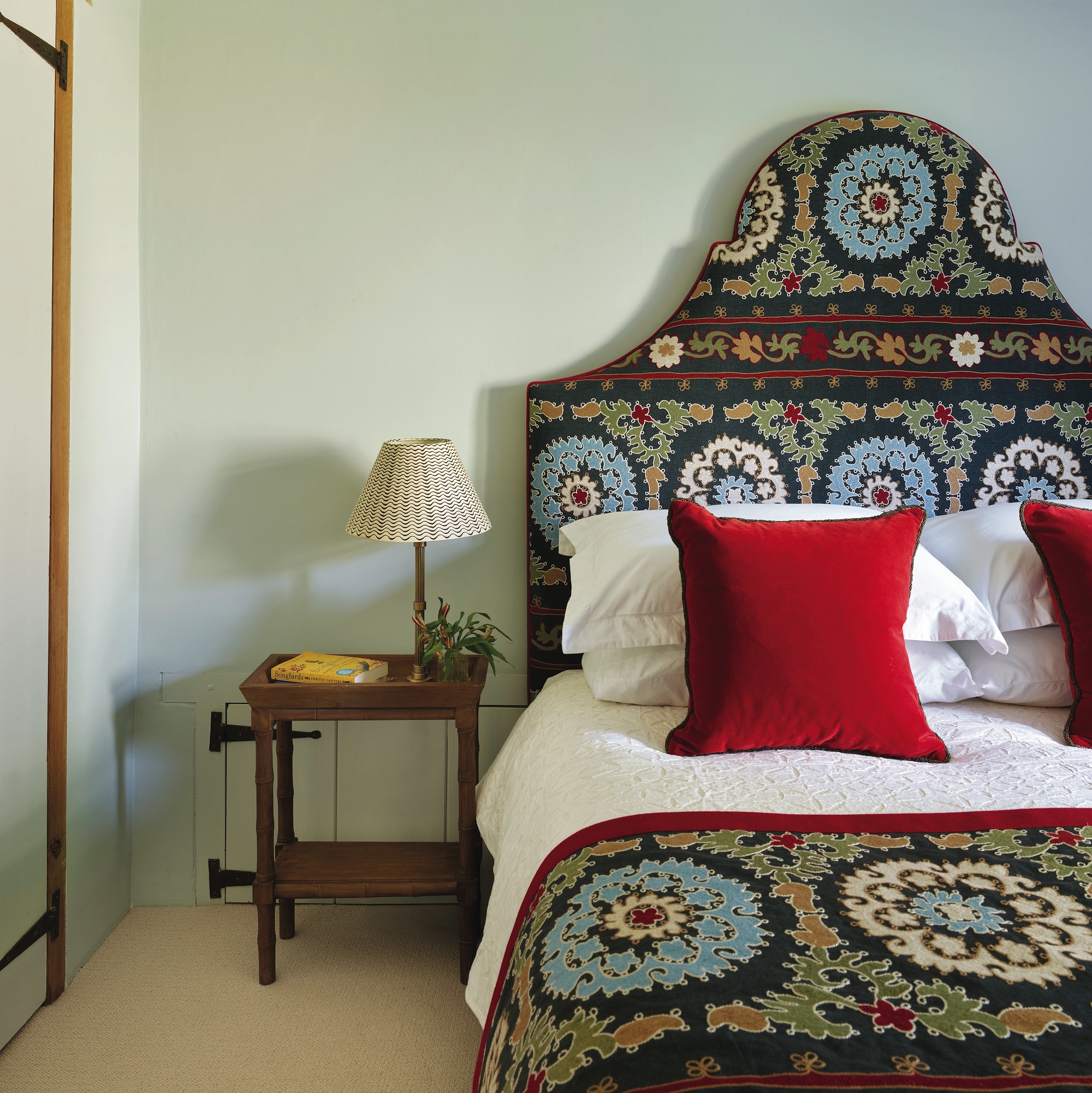 bedroom with upholstered headboard in blue patterned fabric and red cushions on bed