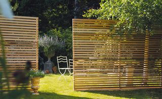 A red cedar gateless slatted fence in a sunny backyard, with a white dining set and trees