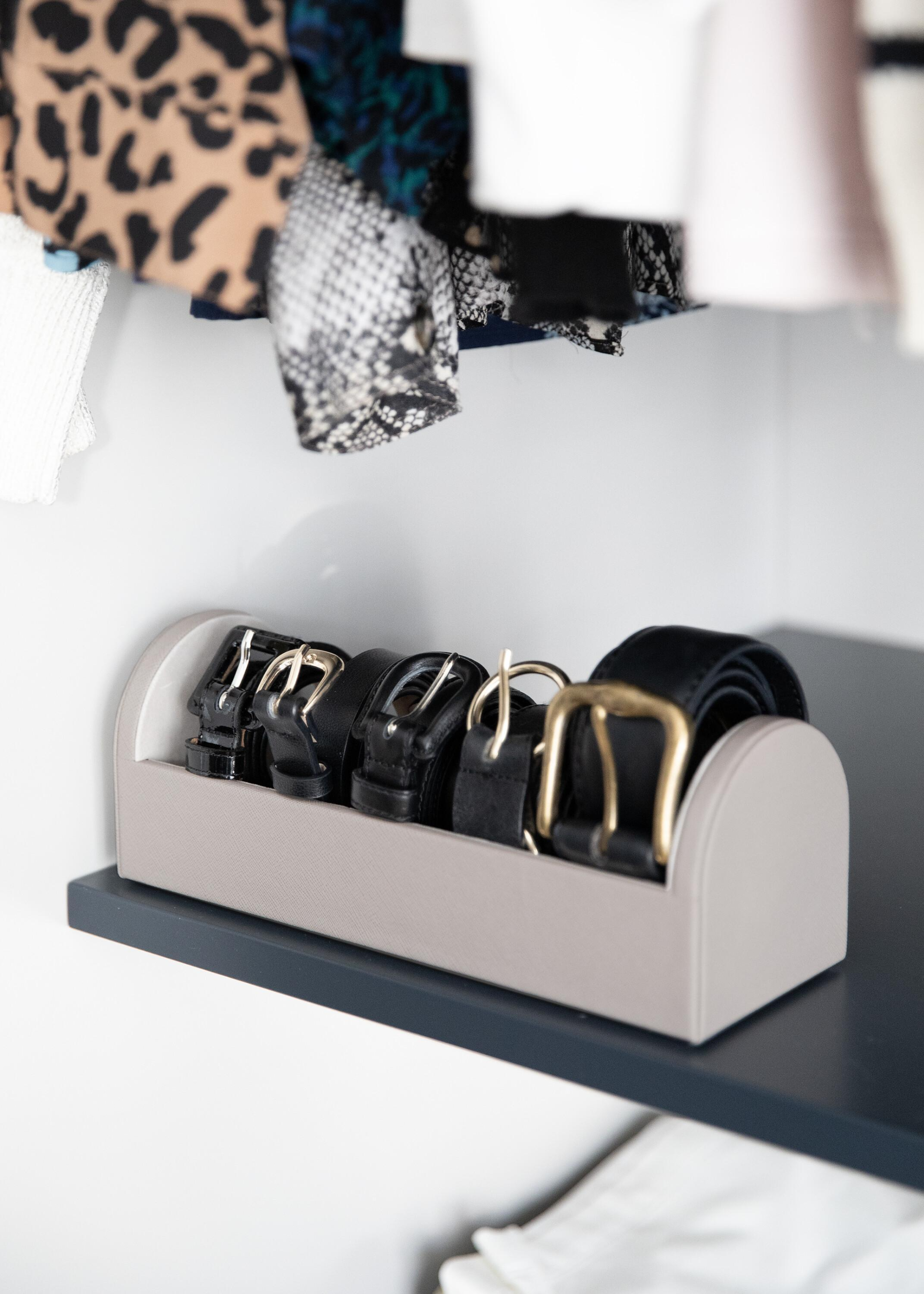 A taupe belt organizer in a closet with five black belts