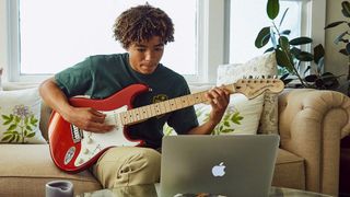 Person playing guitar in front of a Macbook