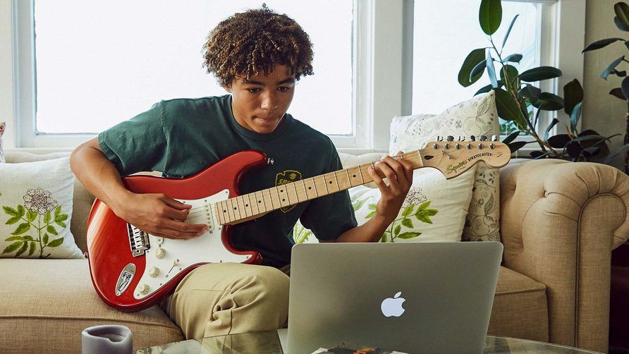 Person playing guitar in front of a Macbook