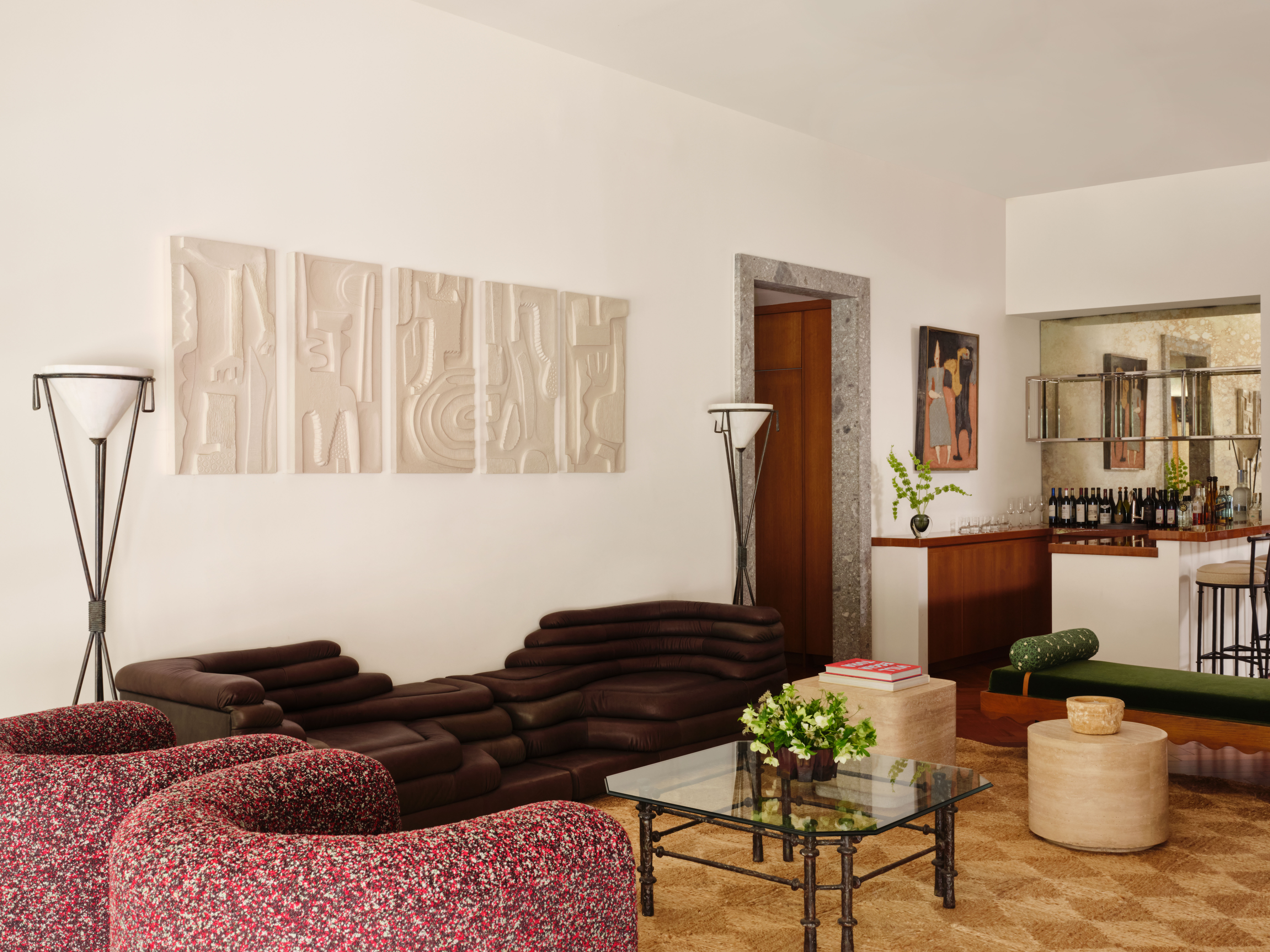 Large living area with mid-century furniture and floor lamps, including a unique, layered chocolate leather sofa, two accent chairs in a multi-colored pattern and a glass coffee table