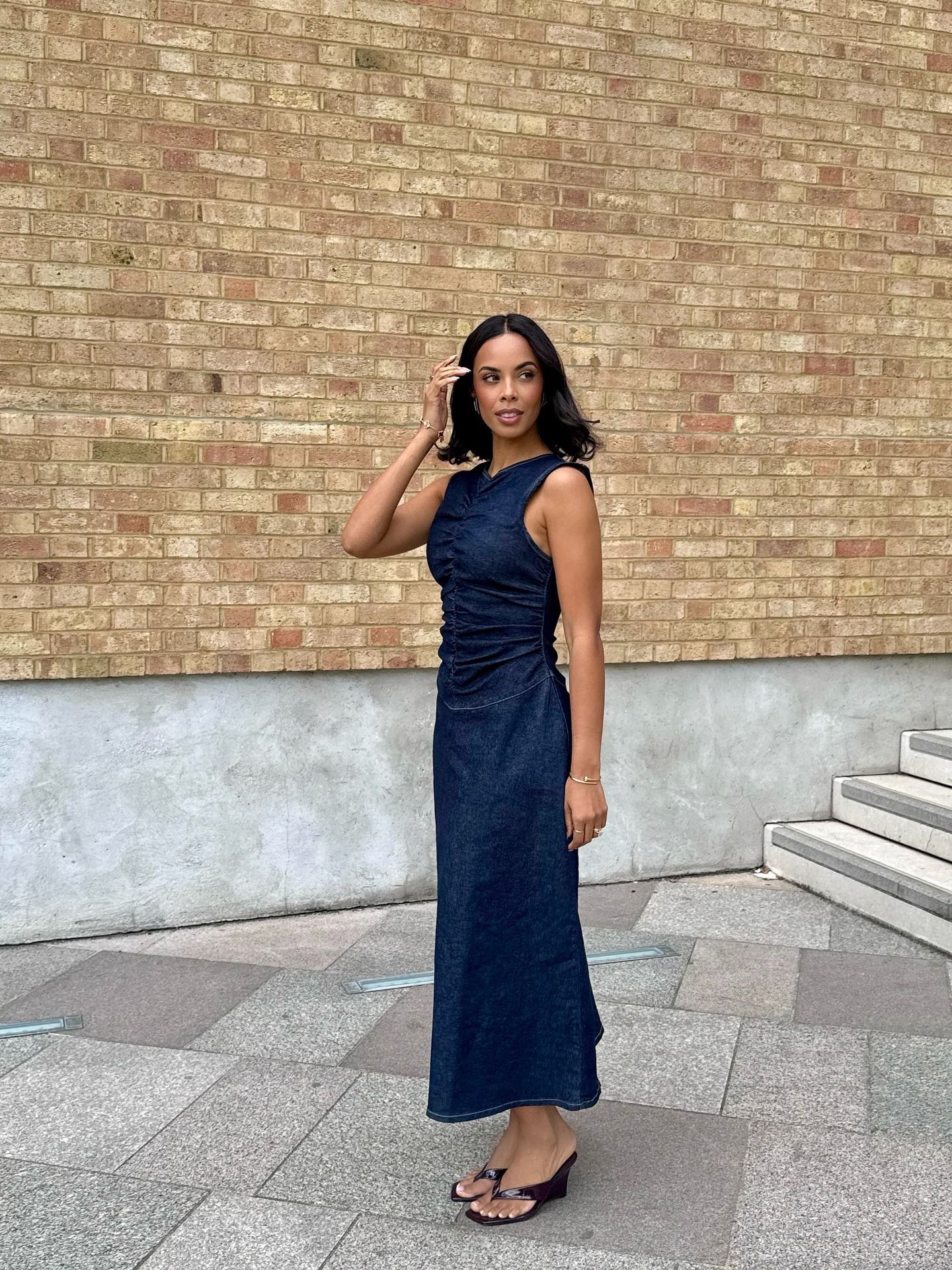 Celeberity Rochelle Humes wears the denim dress trend. She is wearing a sold out ASOS design dress with black wedge kitten heels. She is stood outside the BBC's brown brick wals looking away from the camera in a recent image taken from her Instagram.