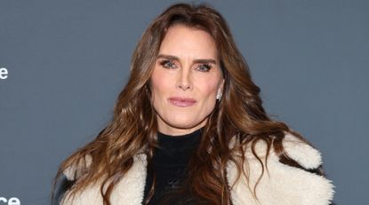 Brooke Shields has long brown wavy hair and wearing a shearling jacket with a black top