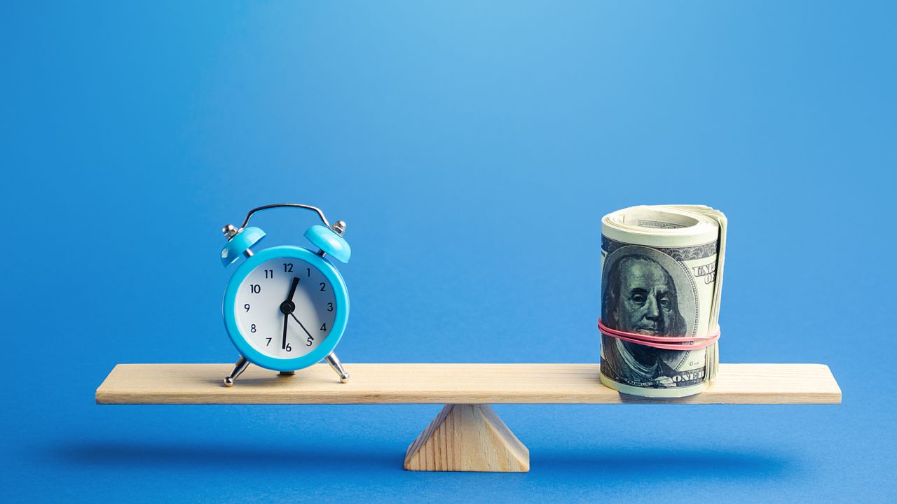 A seesaw with a clock at one end and a roll of cash at the other.