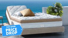 Gold and white Saatva Solaire smart mattress on bed frame against backdrop of blue sea and green plant