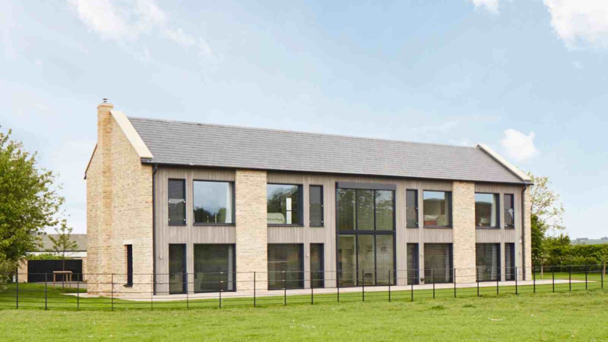 Modern barn-style self build, built by Baufritz and clad in stone. The building overlooks a field.