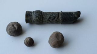 A series of stone balls near a small stone tube with carvings on it, all against a white background