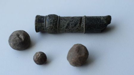 A series of stone balls near a small stone tube with carvings on it, all against a white background