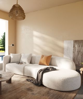 Neutral living room with curvaceous cream sofa, beige painted walls, pendant light, brown rug