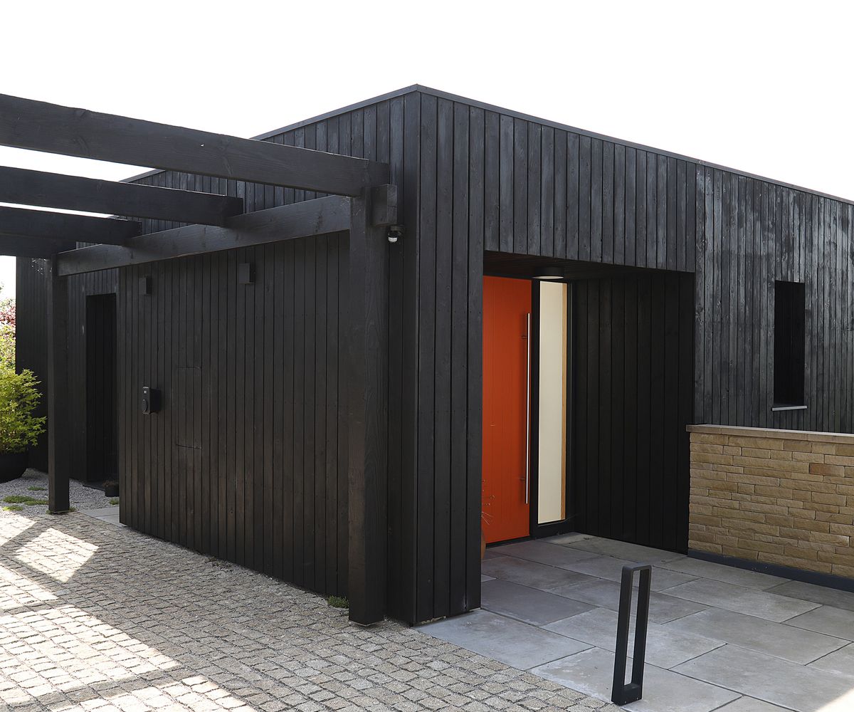 The front driveway and pathway leading to an orange front door. It is a self build home clad in black timber