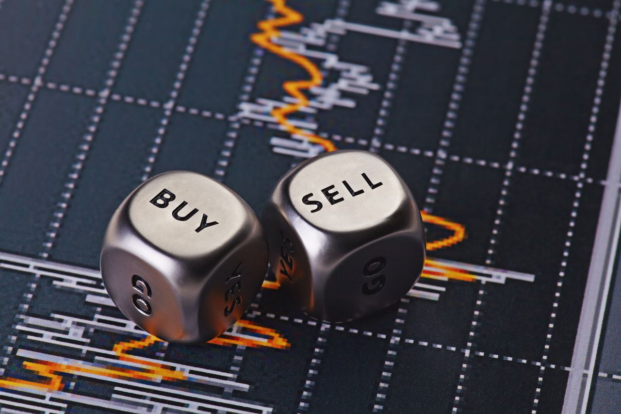 two silver dice with words &quot;buy&quot; and &quot;sell&quot; sitting on top of stock chart